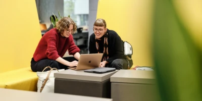 Zwei Studentinnen schauen gemeinsam auf einen Laptop in einer Lounge.